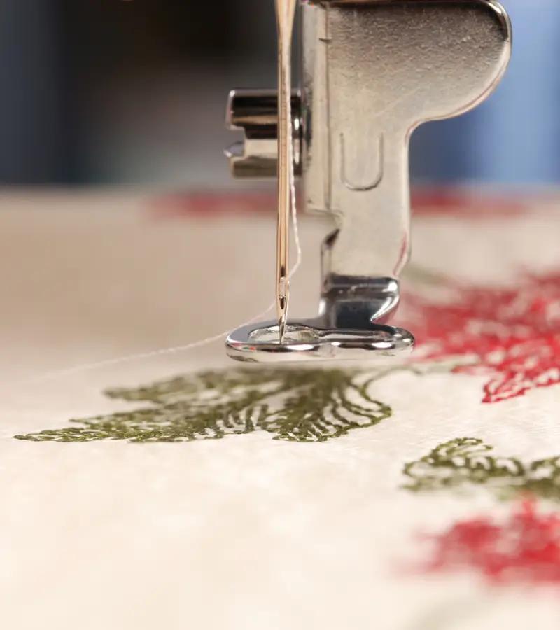 New Project - 2025-02-12T223703.301 Sewing machine needle stitching a fabric with a green and red floral pattern.