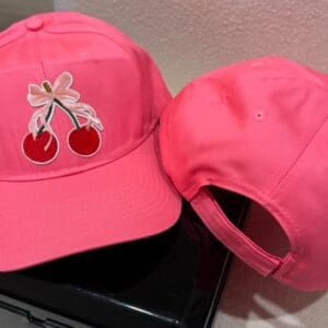 A pink hat with cherries on it sitting next to a laptop.