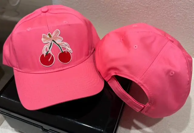 A pink hat with cherries on it sitting next to a laptop.