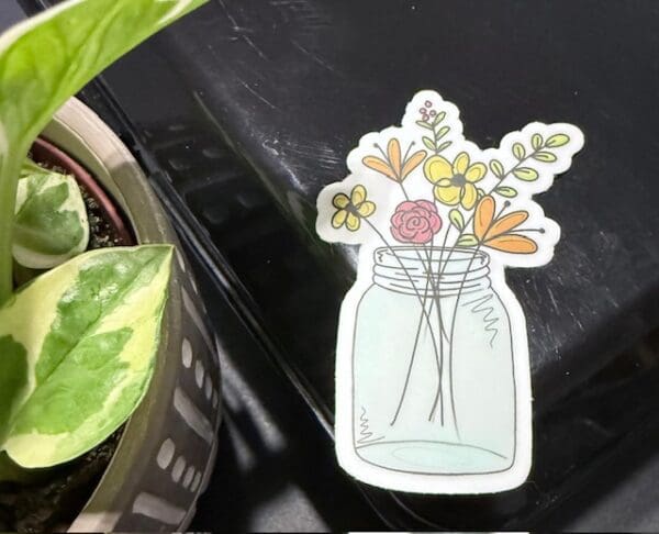A mason jar with flowers in it next to a plant.