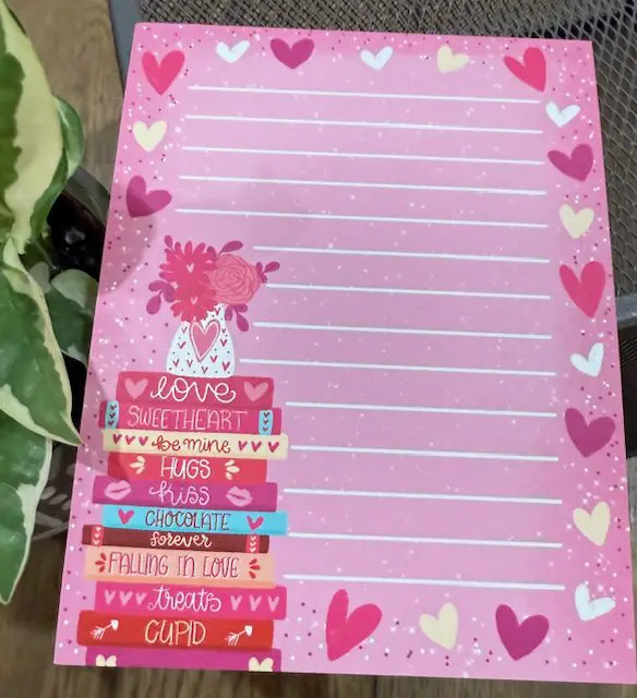 A pink note pad with hearts and flowers on it.