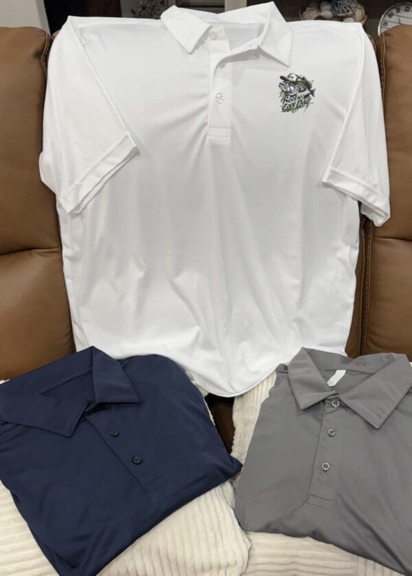 Three shirts are shown on a brown couch.