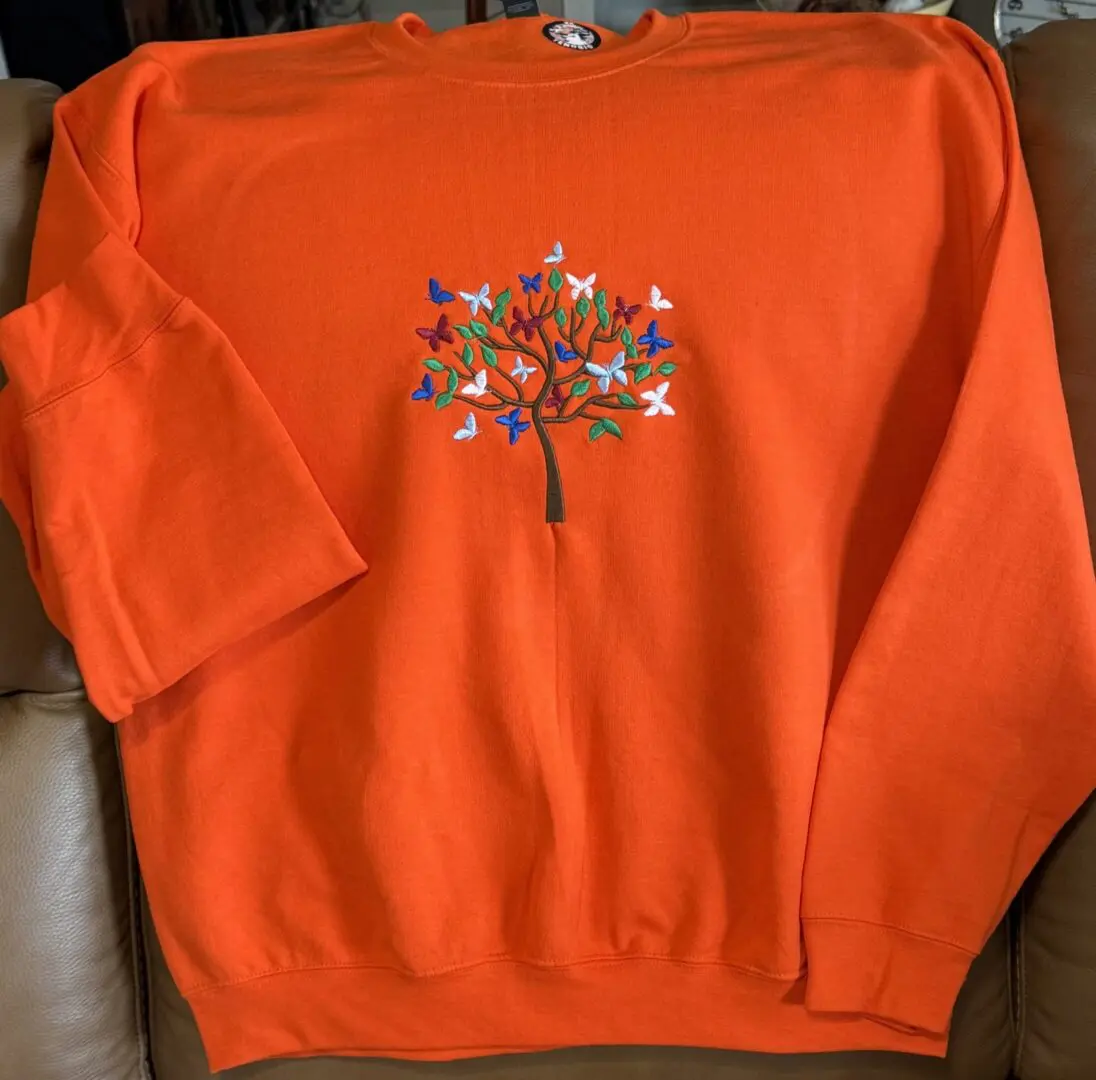 Orange sweater with embroidered tree design.