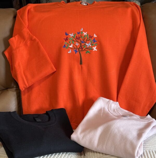 Orange sweatshirt with colorful tree embroidery.