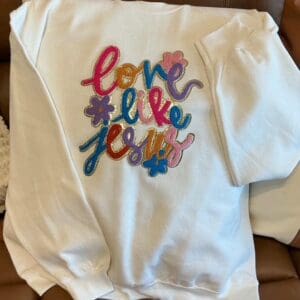 White sweatshirt with "Love Like Jesus" embroidery.