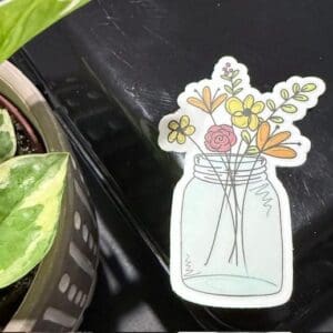 Sticker of flowers in a jar, plant nearby.