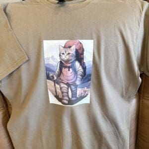 Cat hiker graphic on beige T-shirt.
