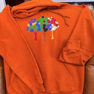 Orange hoodie with colorful tree embroidery.